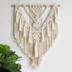 a macrame wall hanging on a white wall next to a potted plant