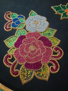 an intricately decorated table top with flowers and leaves on black fabric, surrounded by beads