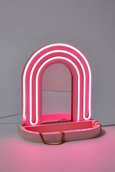 a pink neon sign sitting on top of a white table next to a red purse