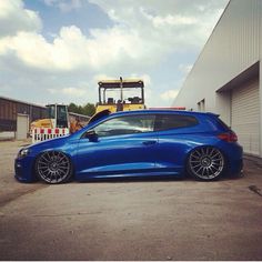 a blue car parked in front of a building with a bulldozer behind it