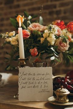 a table topped with a vase filled with flowers and a lit candle next to a sign