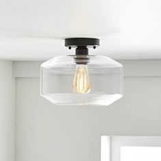 a clear glass light fixture hanging from a ceiling in a room with white walls and windows