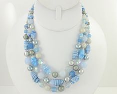 Vintage Blue Glass Bead Necklace. Made in the 1950s, this Baby Blue and Gray Three Strand Beaded Necklace features a beautiful mix of blue, gray, crystal, and white beads. Included are blue striped twisted glass beads, dimpled pale blue glass beads, crystal aurora borealis beads, and gray and white faux pearls. The three strand necklace is finished with lightweight silver tone ends and hook, which is stamped Japan. The necklace is adjustable from 15 to 17 1/2 inches in length. In good vintage condition with minor surface wear consistent with age and some discoloration to the findings. ERA:  Retro, 1950s METAL/MATERIALS:  Alloy,  Glass Bead, Crystal AB Beads, Simulated Pearls HALLMARKS/HISTORY: Japan on hook MEASUREMENTS:  17 1/2 inch in length, with the largest beads 7/8 X 1/2 inch CONDITI Vintage Blue Beaded Necklaces With Spacer Beads, Vintage Blue Necklace With Spacer Beads, Luxury Vintage Blue Beaded Necklaces, Vintage Blue Glass Beaded Necklaces, Vintage Blue Glass Necklace, Lucite Bracelets, Blue Beaded Multi-strand Crystal Necklace, Three Strand Necklace, Rainbow Gemstones