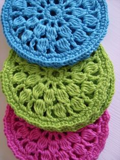 four crocheted coasters are stacked on top of each other in different colors