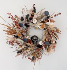 a wreath with dried flowers, leaves and a skull on the front is displayed against a white background