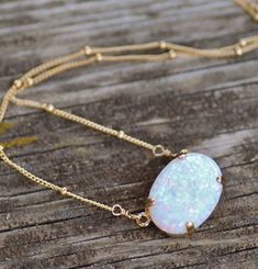 "A stunning necklace made using a lab created opal cabochon. This opal is a lovely shade of white with rainbow fire and flash. The opal is set into a 14K gold filled prong setting and hangs from gold filled satellite style chain. Opal measures 18mm wide (3/4\") or are 14x10mm wide, and is a rounded oval shape. Necklace closes with a gold filled clasp. Please choose desired chain length and opal size at checkout. 18x13mm shown above. Also available in rose gold and silver. Silver will have silver White Opal Birthstone Jewelry, Elegant White Pink Opal Jewelry, Opal Birthstone Necklace With Oval Pendant, Oval Opal Jewelry With Natural Stones, White Oval Opal Necklace, White Ethiopian Opal Gemstone Jewelry, Opal Gemstone Oval Pendant Necklace, Opal Oval Pendant Jewelry For Gift, Adjustable Oval Opal Jewelry