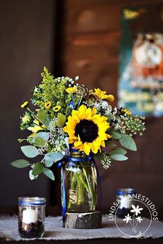 a vase with sunflowers and greenery is sitting on a table next to two jars