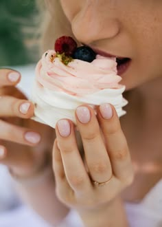 a close up of a person eating a cupcake with whipped cream and berries on top