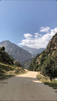 a dirt road in the middle of mountains with trees on both sides and rocks to the side