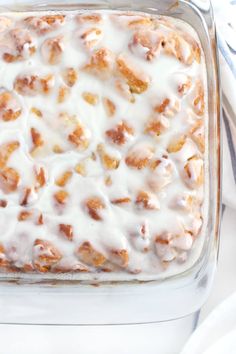 a glass casserole dish filled with cinnamon rolls covered in icing on top of a white table cloth