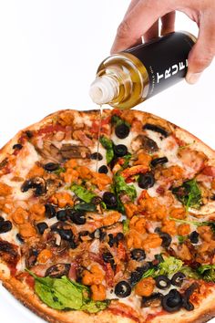 a person is pouring olives onto a pizza