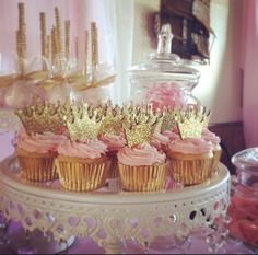 cupcakes with pink frosting and gold crown decorations on a white cake stand