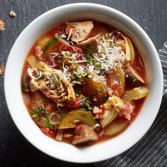 a white bowl filled with vegetable soup on top of a black table next to a spoon