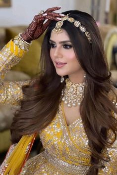 a woman in a yellow outfit with long hair and jewelry on her head, wearing a gold