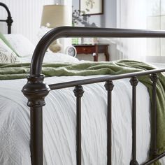 a metal bed frame with green blankets and pillows on it's headboard in a bedroom