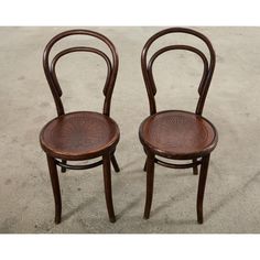 two wooden chairs sitting next to each other on top of a cement floor covered ground