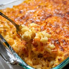 a spoon full of macaroni and cheese in a glass casserole dish