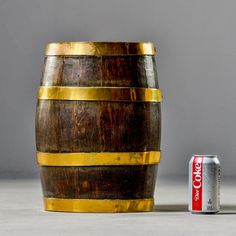 a wooden barrel next to a can of coca - cola on the ground with a gray background