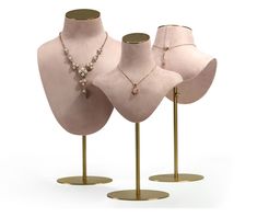 three pink mannequins with necklaces on gold stands against a white background