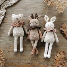 three crocheted stuffed animals sitting next to each other on a wooden table with leaves