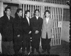 a group of men standing next to each other in front of jail cell doors with bars behind them