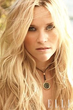 a woman with long blonde hair and blue eyes looking at the camera while wearing a necklace