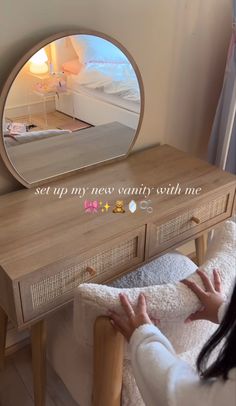 a woman looking at her reflection in a round mirror on a wooden table next to a bed