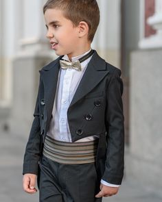 a young boy in a suit and bow tie walks down the street with his hands in his pockets