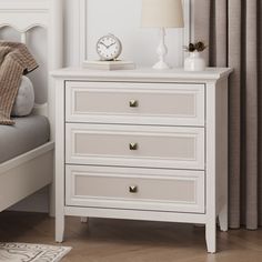 a white nightstand with two drawers and a clock on top of it next to a bed