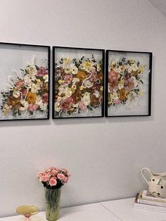 three framed pictures on the wall above a table with flowers in vase and teddy bear