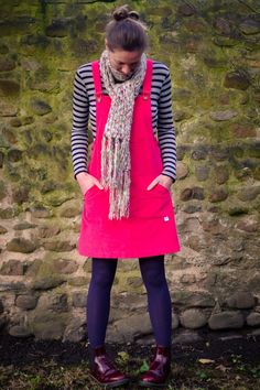 a woman wearing an apron and scarf standing in front of a stone wall with her hands on her hips