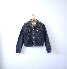 One vintage 1990's dark denim jacket, Express jean jacket, women's size small - Pointed collar. - 6 button closures going down the center front of the jacket. - 2 chest pockets with flaps and button closures. 2 slide pockets on the front of the jacket. - 1 button on each wrist cuff. - 2 tabs on the back of the waistband with 2 adjustable buttons. - Shorter, feminine fit through the torso. - Thick 100% cotton. Not broken in. - Color scheme: dark blue denim. Silver toned hardware. | CONDITION | A+ Vintage Dark Wash Button-up Denim Jacket, Dark Wash Cotton Denim Jacket With Buttons, Fitted Button-up Denim Jacket, Fitted Denim Blue Jacket For Fall, Trendy Fitted Denim Jacket With Snap Buttons, Retro Fitted Button-up Denim Jacket, Retro Button-up Denim Jacket For Winter, Dark Wash Button-up Denim Jacket For Fall, Retro Fitted Denim Jacket With Button Closure