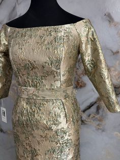 a gold dress on a mannequin head stand in front of a marble wall