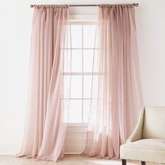 a chair sitting in front of a window next to a white wall with curtains on it