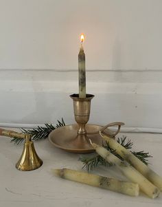 a lit candle is sitting on a plate next to some candlesticks and pine needles