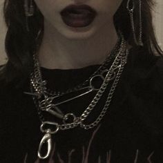 a woman with black lipstick and chains on her neck holding a cell phone up to her ear