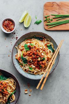 two bowls filled with noodles and vegetables next to chopsticks