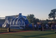 an inflatable water slide on the side of a field with people standing around it