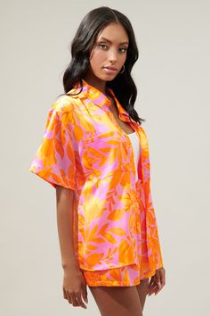 Brb, off to somewhere tropical with a drink in hand. The ideal vacation button up is here. A bright pink and orange tropical print decorates the Otto shirt. A classic collared top with a functional button front. It maintains a relaxed boyfriend fit and can easily be paired with your favorite bottoms or make it a set with the matching shorts.- Satin- Boyfriend fit- Pockets- Functional buttons- Color: Orange MultiSize + Fit - Model is 5'10" and wearing size XS- Measurements taken from size S - Che Orange Collared Tops For Summer, Spring Collared Camp Shirt With Hibiscus Print, Orange Short Sleeve Shirt For Vacation, Pink Collared Hawaiian Shirt For Beach, Pink Hawaiian Shirt For Summer, Orange Short Sleeve Hawaiian Shirt For Spring, Pink Collared Hawaiian Shirt For Vacation, Orange Collared Camp Shirt For Summer, Orange Vacation Shirt For Spring