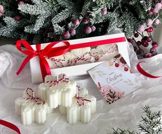 some white candles are sitting in front of a christmas tree with red ribbon on it