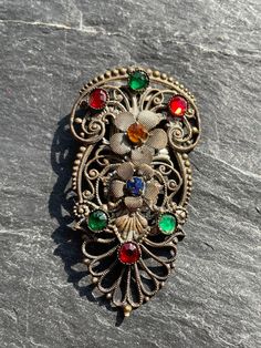 A rare clip it was my grandmothers mother's, it is a scarf clip adorned with green, red, Amber, and blue glass stones, these are all set on an intricate metal base, it has flowers in metal, it is unsigned so difficult to date but I would estimate it to be around late 1920's late 1930's of course it is possible that it could be older but judging by the design of the clip about 1930's. On my limited research it looks like to could be Czech which would go with the 1930's. The metal is a little dull Bohemian Multicolor Brooch Jewelry, Antique Jeweled Brooches As Gift, Ornate Jeweled Brooches As Gifts, Ornate Jeweled Brooches For Gifts, Antique Clip-on Brooches As Gifts, Antique Clip-on Brooches For Gifts, Antique Clip-on Brooches As A Gift, Antique Clip-on Brooch Gift, Antique Multicolor Brooch Jewelry