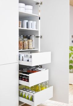 an organized pantry in the corner of a room with white cupboards and open drawers