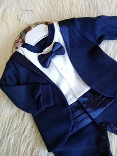 "This charming baby tuxedo is the perfect outfit for any special occasion. Made from high-quality cotton fabric, the navy blue tuxedo features a detachable bow tie and a satin-covered belt and inside vest. The one-piece snapsuit has an attached vest on it, making it easy to dress your little one. Whether you're looking for a wedding outfit, christening outfit, or baptism outfit, this baby tuxedo is perfect for your adorable little man. Handmade with care and attention to detail, this baby tuxedo Elegant Fitted Suits For Baptism, Elegant White Suits For Baptism, Elegant Fitted Suit For First Communion, Elegant Blue Baptism Dress For Party, Classic Fitted Suit For Baptism, Elegant Fitted Blue Baptism Dress, Fitted White Sets With Bow Tie, White Fitted Sets With Bow Tie, Elegant Blue Sets For Baptism