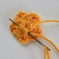 the crochet flower is being worked on with two knitting needles, which are yellow and orange