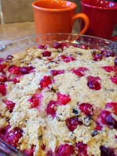 a pie with cranberries and other toppings in a glass dish next to two mugs