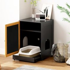 a cat litter box sitting on top of a wooden floor next to a potted plant