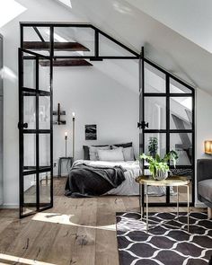 an attic bedroom with white walls and wood flooring, black framed glass doors leading to the bed