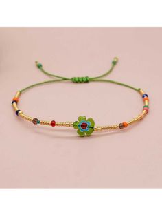 the bracelet is decorated with beads and flowers on green string, which are attached to a gold - plated cord