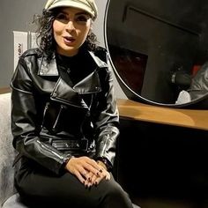 a woman sitting on top of a chair in front of a mirror and wearing a hat