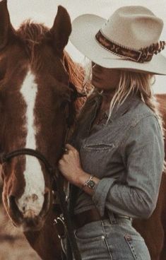 a woman wearing a cowboy hat standing next to a horse